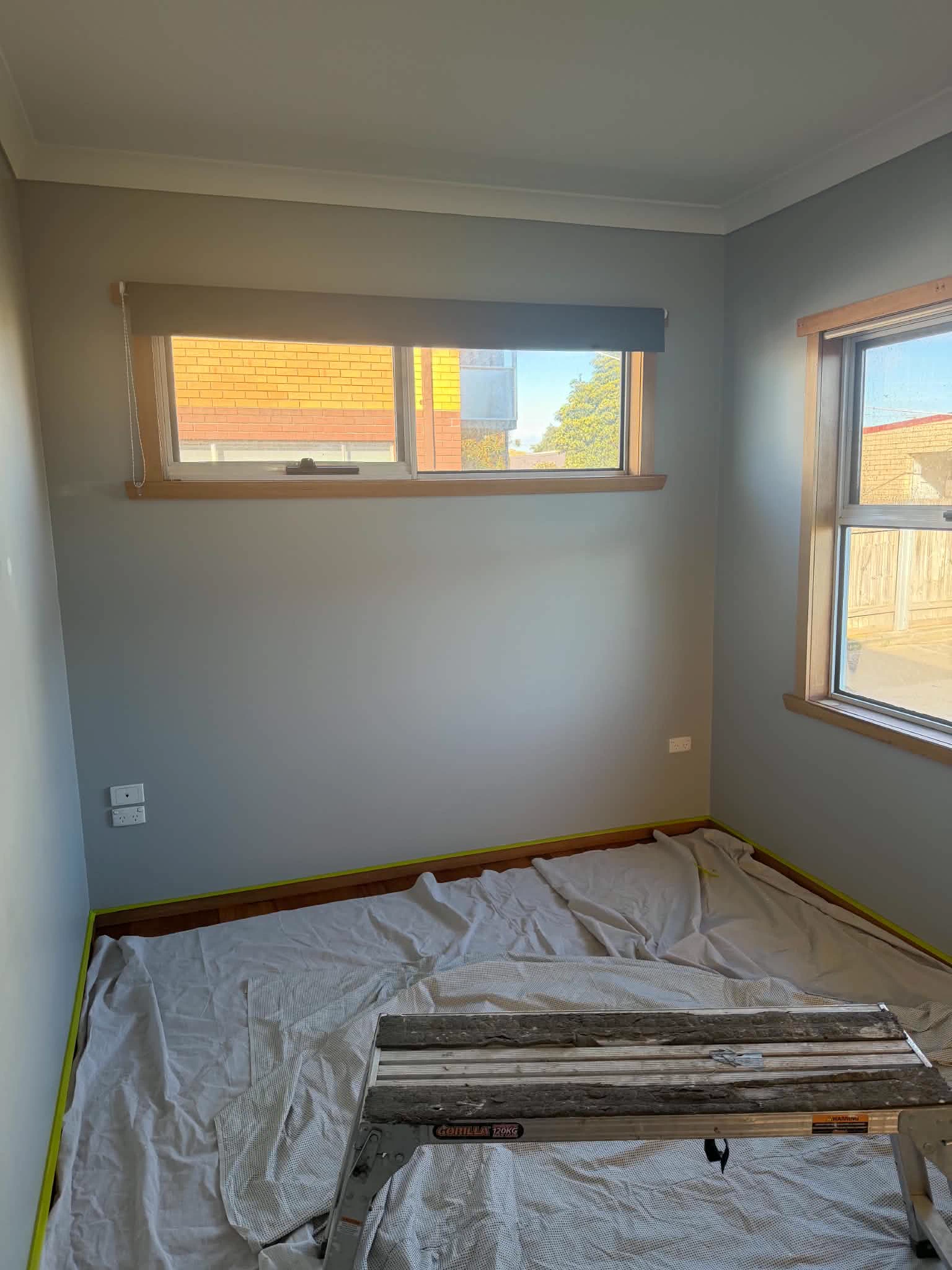 Bedroom before the repaint: grey walls, floor covered and edges taped